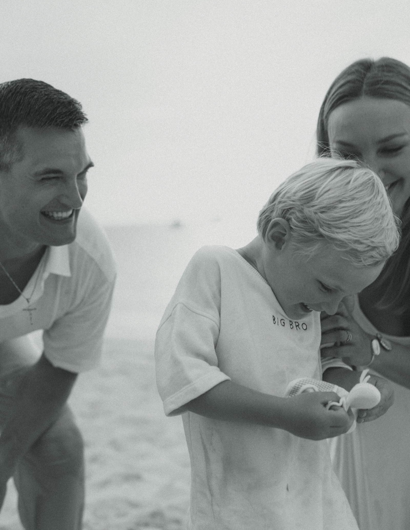 Their son in a Big Bro shirt, examining a shell with his parents