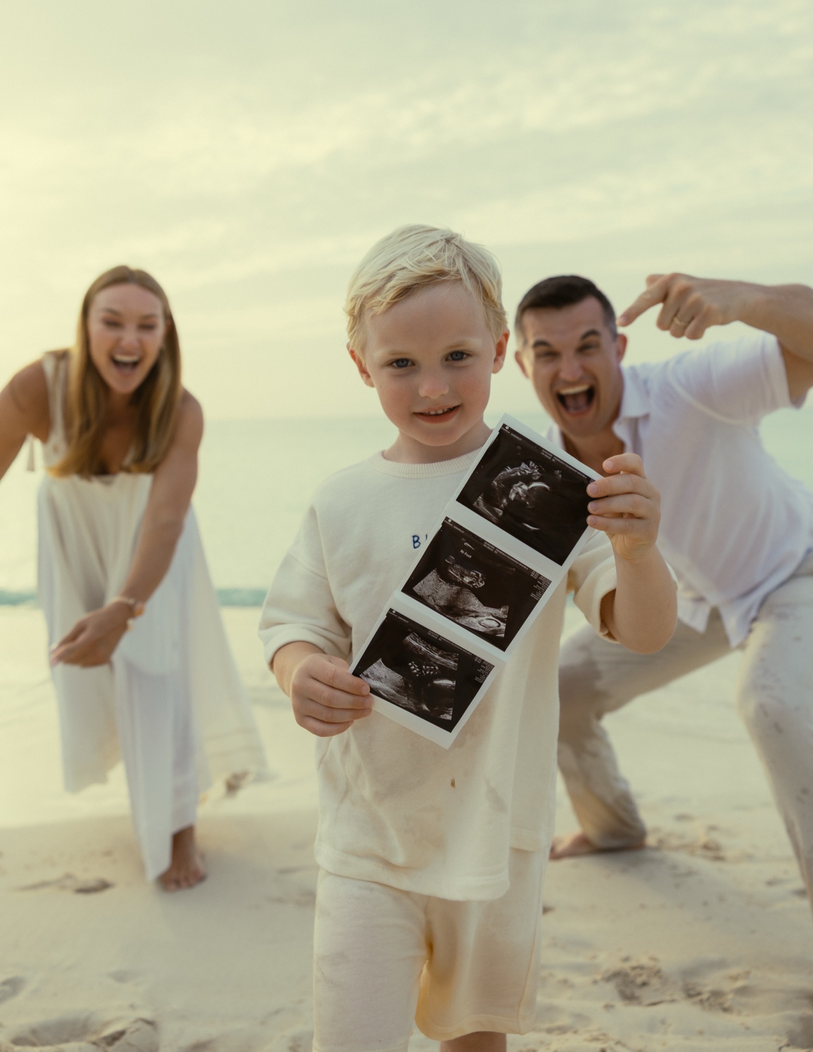 Their son holding ultrasound photos on the beach while his parents celebrate